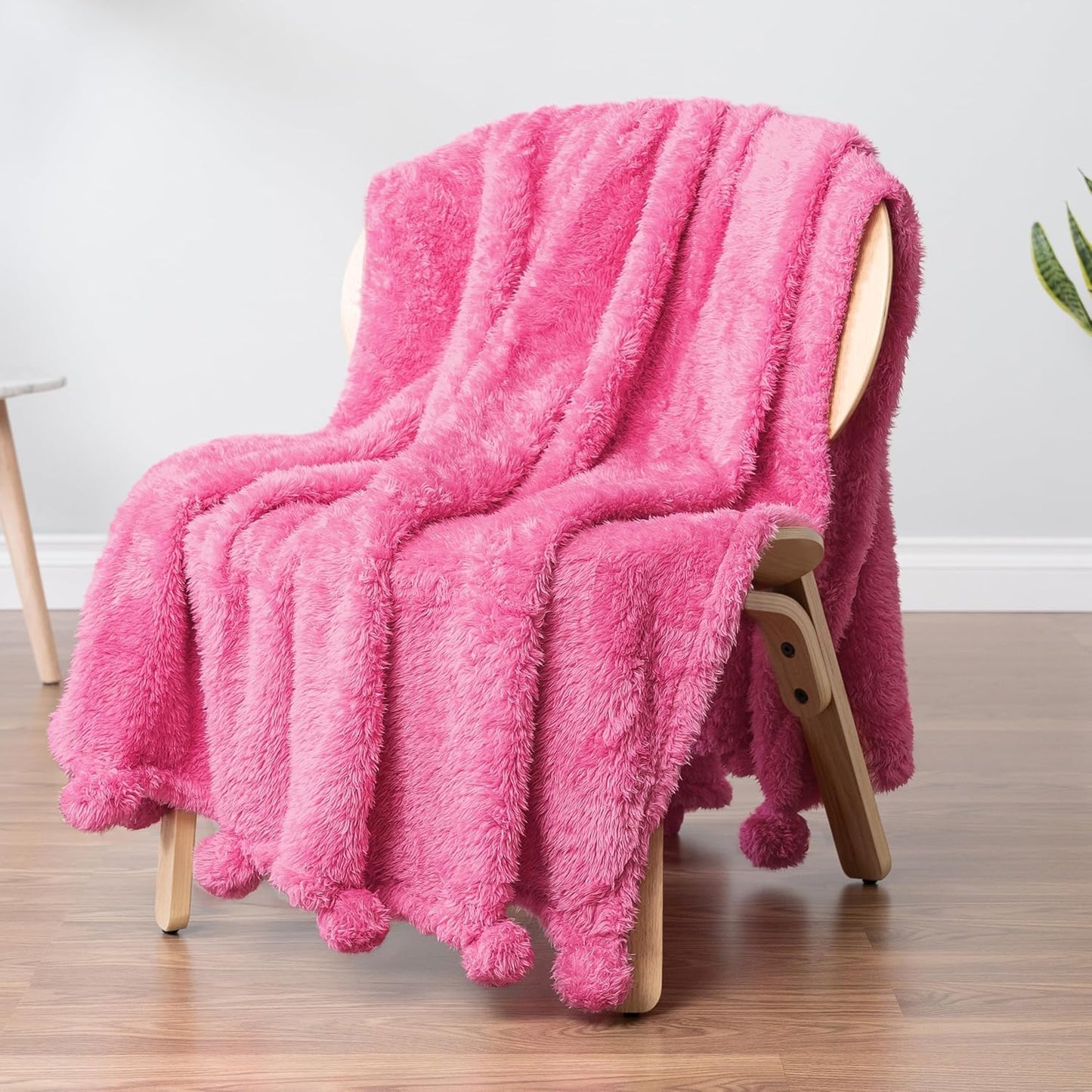 Pink fluffy dorm preppy throw blanket draped over a wooden chair on a wooden floor.