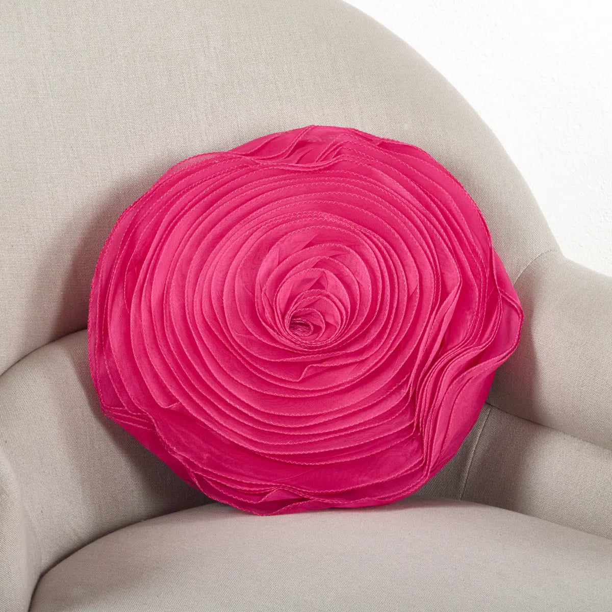 Round hot pink rose throw pillow with layered satin petals on a cream armchair, perfect for glam or coquette dorm décor